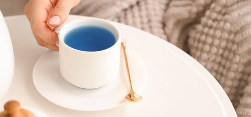 Woman taking cup of tasty blue tea at home. Closeup