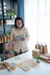 Mature asian woman business owner E-commerce online orders with tablet entrepreneurship jewellery accessories handcraft Cardboard Box.