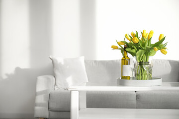 Beautiful vase of yellow tulips with bottle of wine and glasses on coffee table in living room
