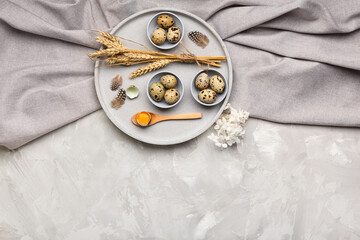 Bowls with fresh quail eggs, feathers and wheat on grey background