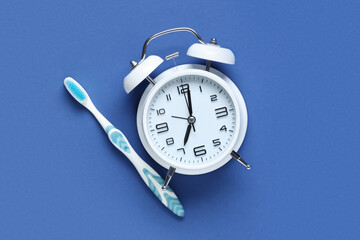 Alarm clock and toothbrush on blue background