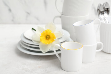 Beautiful tableware with daffodil on white table near marble wall