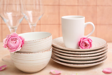 Beautiful tableware and roses on table near orange tile wall