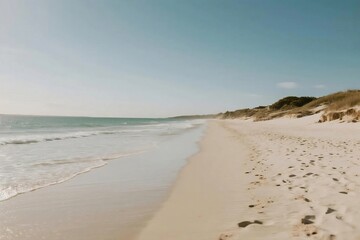 Wide Sandy Beach with Gentle Waves and Dunes under Clear Blue Sky