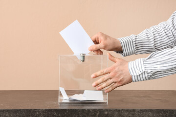 Voting man near ballot box on table against beige background