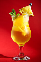 Glass of tasty cocktail with pineapple and orange on red background