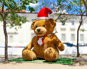 A large teddy bear outdoors wearing a Santa hat with a blurred background