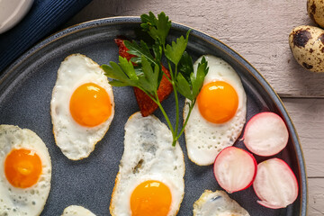 Plate with fried quail eggs, radish and parsley on grey wooden table, closeup