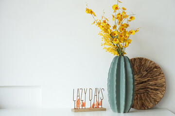 Vase with artificial flowers and decor on table near light wall
