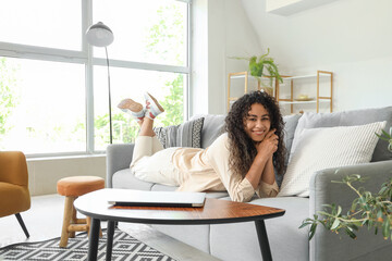 Young African-American woman lying on grey sofa at home