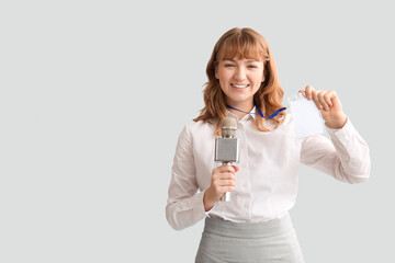 Young happy female reporter with microphone and blank ID badge on grey background