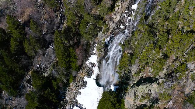 Aerial view of the snowed forest and mountains around a beautiful waterfall La Ratera in the Spanish Pyrenees.