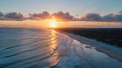 Sunrise over a serene tropical beach with gentle ocean waves and golden light reflecting on the water. Aerial drone view of the coastline at dawn with scattered clouds and calm atmosphere.