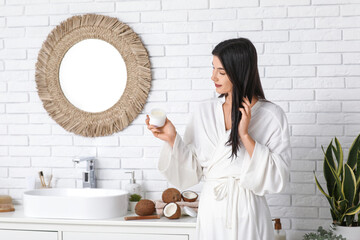 Beautiful young woman applying coconut oil onto hair in bathroom