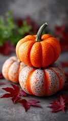 Stacked decorative orange speckled pumpkins with autumn leaves on a stone tabletop. Fall harvest season decoration for holiday.