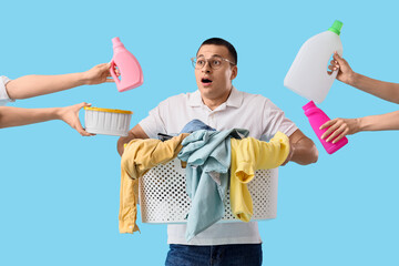 Surprised young man holding laundry basket and hands with bottles of detergent on blue background