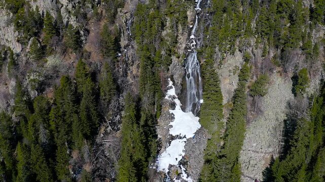 Aerial view of the snowed forest and mountains around a beautiful waterfall La Ratera in the Spanish Pyrenees.