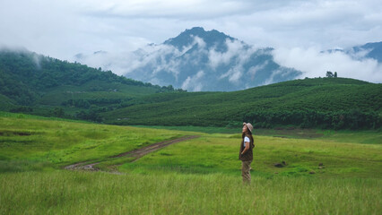 A woman traveling in green field and mountains on cloudy day