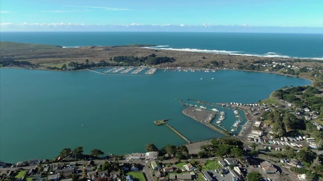 Aerial view of houses in a coastal town of Bodega Bay, California, USA, nestled between the ocean and rolling hills, showcasing a peaceful residential community.