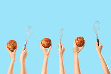 Female hands with tasty buns and whisks on blue background