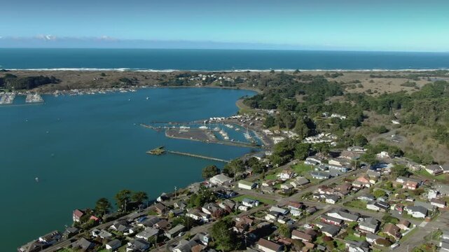 Aerial view of houses in a coastal town of Bodega Bay, California, USA, nestled between the ocean and rolling hills, showcasing a peaceful residential community.