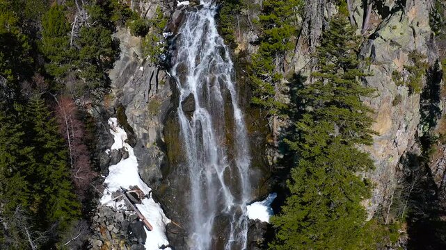 Aerial view of the snowed forest and mountains around a beautiful waterfall La Ratera in the Spanish Pyrenees.