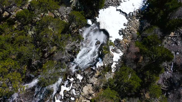 Aerial view of the snowed forest and mountains around a beautiful waterfall La Ratera in the Spanish Pyrenees.