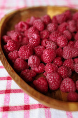 A wooden bowl with ripe raspberries lies on a rustic tablecloth.
