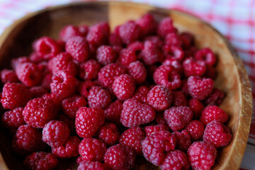 A wooden bowl with ripe raspberries lies on a rustic tablecloth.