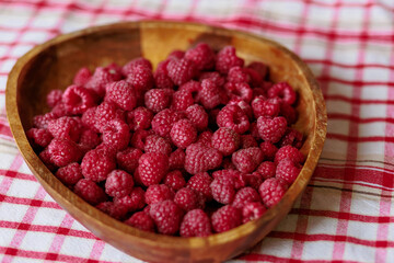 A wooden bowl with ripe raspberries lies on a rustic tablecloth.