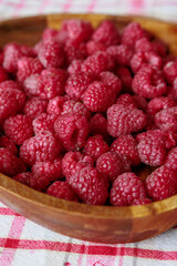 A wooden bowl with ripe raspberries lies on a rustic tablecloth.