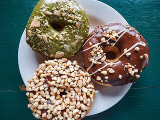 3 donuts on a plate, chocolate peanut and green tea donuts on the table, green background, top...