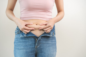 Belly, chubby, obese asian young woman hand holding, pinching excess fat belly with finger and wear tight jeans, show fat abdomen on body, getting loss weight. Diet lifestyle and health care concept.