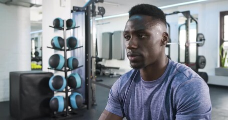 African American man sipping water from water bottle on gym bench after workout, catching breath - Powered by Adobe
