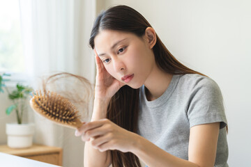 Problem hair, stressed beautiful asian young woman, girl hand holding comb show hairbrush with hair loss in brush after brushing fall near mirror at home. Health care, beauty with treatment concept.