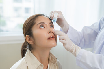 Health care concept, eye doctor eye drops to asian young woman patient, hand using medical eye drop to treat dry eye, suffering irritation or inflammation, allergy optical symptom at optic clinic.
