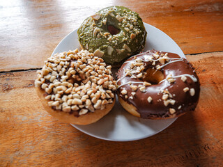 Three donuts served in white plate with various flavor. peanut, chocolate and matcha, side view with brown background