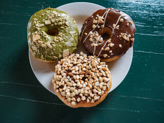 3 donuts on a plate, chocolate peanut and green tea donuts on the table, green background, top...