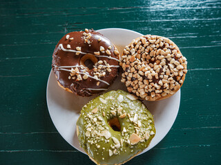 3 donuts on a plate, chocolate peanut and green tea donuts on the table, green background, top...