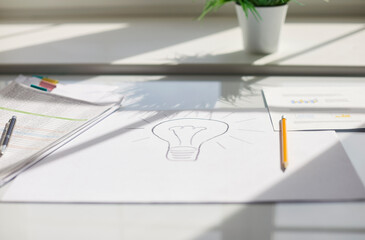 Closeup of drawing with pencil light bulb on white sheet of paper lying at the desk in modern...