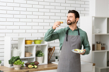 Handsome man eating toast with avocado in kitchen