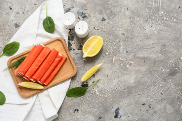 Wooden board with tasty crab sticks, cut lemon and spinach leaves on grey background © Pixel-Shot