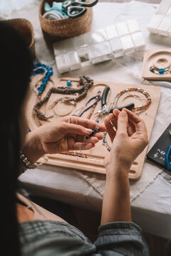 Close up of hands woman jewelry designer. She is sitting at a workspace with tools on it and is creating jewelry by stringing beads on fishing line. The process of creating jewelry. Small business. 