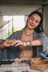 Portrait of a young brunette woman jewelry designer. She is sitting at a work table on which lie...