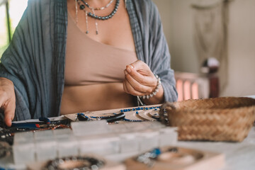 Close up of hands woman jewelry designer. She is sitting at a workspace with tools on it and is...