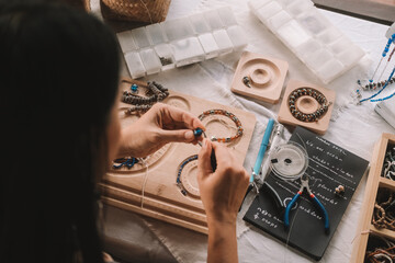 Back view of a young brunette woman, a jewelry designer. She is sitting at her workspace, where she...
