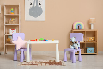 Interior of children's room with lamp, many toys in shelving units and play table near beige wall
