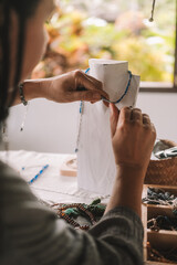 Close up of hands of a woman jewelry designer. She is sitting at the workspace trying on necklaces she has created on a mannequin. Jewelry making process. Small home business. Startup.