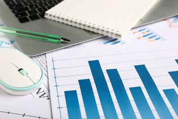 Laptop with computer mouse, notebook, many business graphics and diagrams as background, closeup