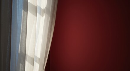 crimson background | Soft sunlight filters through sheer white curtains, casting delicate shadows on a rich red wall, creating a serene and inviting atmosphere in a cozy interior